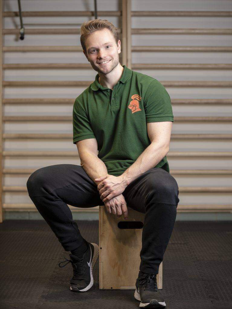 Shopfoto Polo Personal Trainer Jakob Ritter sitzt auf einem Hocker vor einer