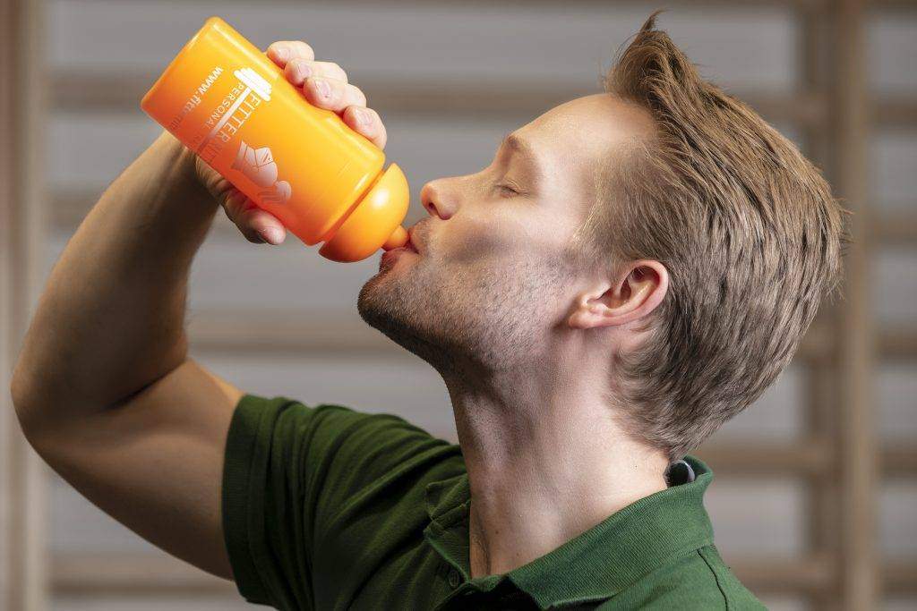 Shopfoto Trinkflasche Personal Trainer Jakob Ritter trinkt aus einer orangenen Trinkflasche mit weißem fitterritter Logo.